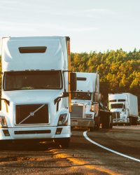 Three semi trucks driving on a highway through a forested landscape in Arizona.
