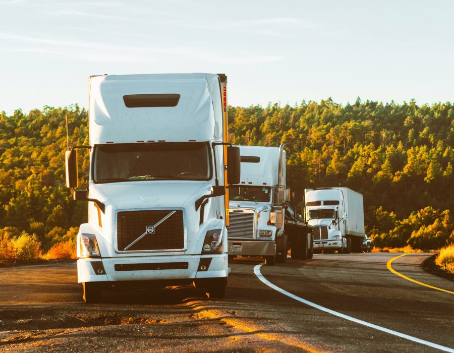Three semi trucks driving on a highway through a forested landscape in Arizona.